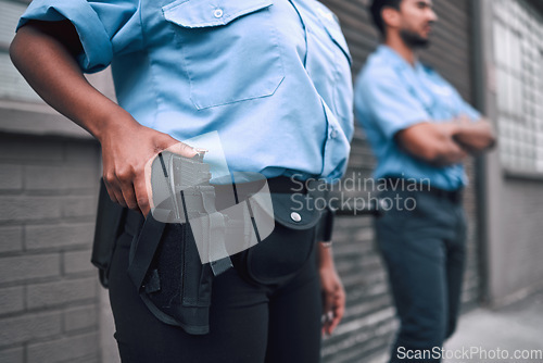 Image of Hand, gun and security with a police officer on duty or patrol in the city for safety and law enforcement. Legal, service and armed response with a guard outdoor in an urban town for crime prevention