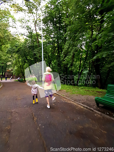 Image of Mother and little curly toddler girl walking together in a park on a wet summer day after rain, view from the back