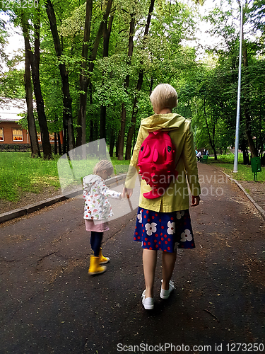 Image of Mother and little curly toddler girl walking together in a park 