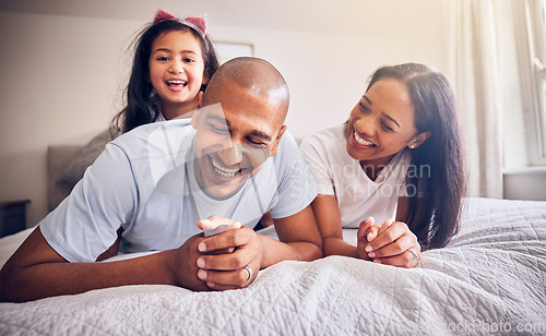 Image of Family, relax and happy on a bed at home while laughing and playing for funny quality time. Man, woman or parents and a girl kid together in the bedroom for morning bonding with love and care