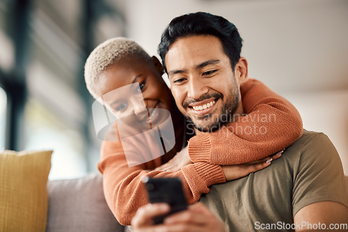 Image of Phone, interracial couple and technology on a sofa at home reading text in a living room. Support, young people and hug together in a house sitting on a lounge couch with mobile streaming and video