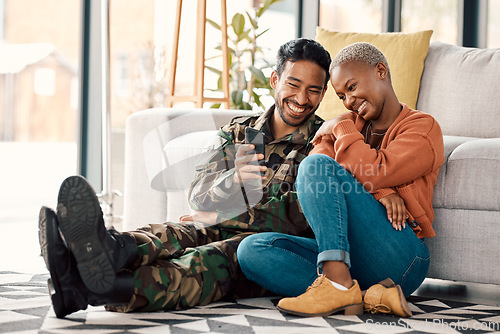 Image of Army man, interracial couple and return with phone video on a sofa at home with love and care. Lounge, young people and mobile scroll in a house sitting on ground relax with travel picture of soldier
