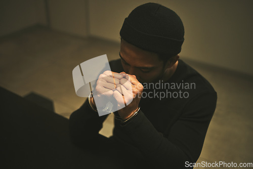 Image of Interrogation, worry and criminal with handcuffs in jail for investigation, stealing and theft in station. Arrested suspect, law and man praying with anxiety, worry and scared in prison for crime