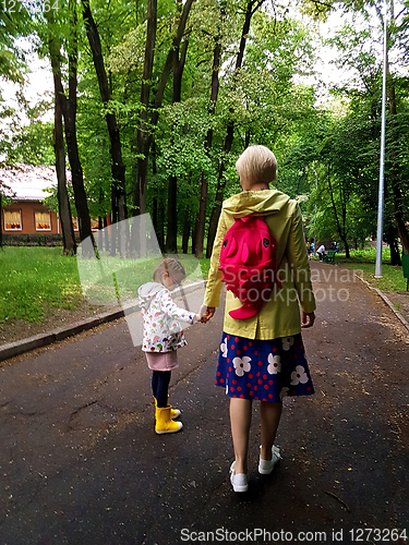 Image of Mother and little curly toddler girl walking together in a park 