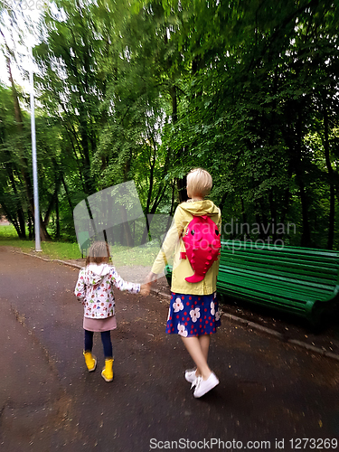 Image of Mother and little curly toddler girl walking together in a park 