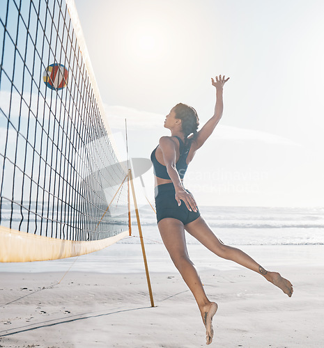 Image of Woman, jump and volleyball on beach by net in serious sports match, game or competition. Body of female person jumping for ball in volley for spike, fitness or healthy wellness in exercise by ocean