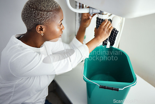 Image of Plumbing, water and a black woman in the bathroom of her home with a cloth and bucket waiting for assistance. Sink, emergency and burst pipe with a young female homeowner in her house to stop a leak