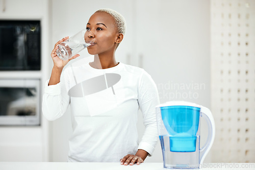 Image of Woman, filter and drinking water for health at home for a healthy lifestyle, diet and nutrition. Young african person with a glass from a container or pitcher in a kitchen for detox and wellness