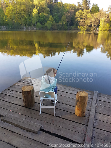 Image of lonely little child fishing from wooden dock on lake