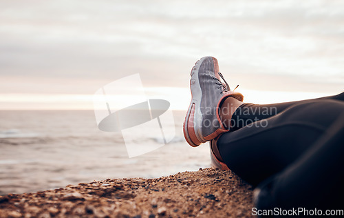 Image of Fitness, shoes and sea in nature relax with freedom outdoor sitting. Waves, ocean and water with a person and athlete taking a break from training and workout with feet in sunset with mockup space