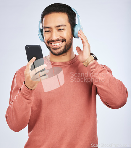 Image of Man, headphones and smartphone for music in studio, white background and podcast app. Happy asian male model, cellphone and listening to audio, streaming mobile sound and online radio media with tech