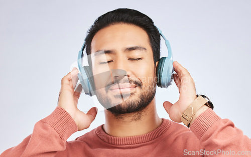 Image of Man, headphones and calm music in studio, white background and podcast for peace. Face of happy young asian male model listening to audio, streaming sound and hearing radio to relax with song in mind