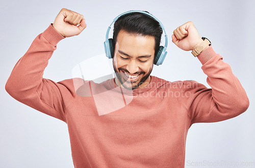 Image of Man, headphones and dance to music in studio, white background and celebrate with energy. Happy, excited and young asian male model listening to audio, streaming sound and hearing rave song on radio