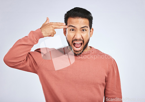 Image of Portrait, angry and asian man with hand gun in studio for suicide, threat or shooting warning on grey background. Screaming, stress and face of male person with anxiety, self harm or bipolar crisis