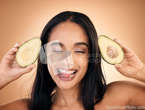 Image of Face, tongue out and woman with avocado for skincare isolated on a brown background in studio. Fruit, funny and happy model with food for nutrition, health or vegan diet, omega 3 or natural cosmetics