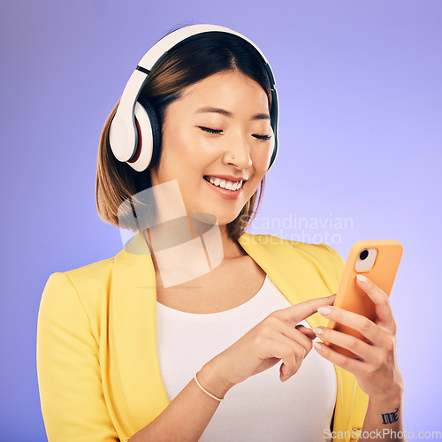 Image of Headphones, music and happy Asian woman with phone in studio for social media, subscription and radio. Female person on smartphone listening to audio, song and track on purple background to relax