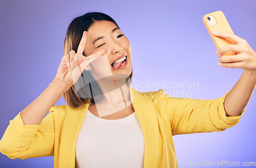 Image of Asian woman, peace sign and funny face for selfie, photo or memory against a purple studio background. Happy female person or model pose with peaceful emoji, goofy or silly for picture or online vlog