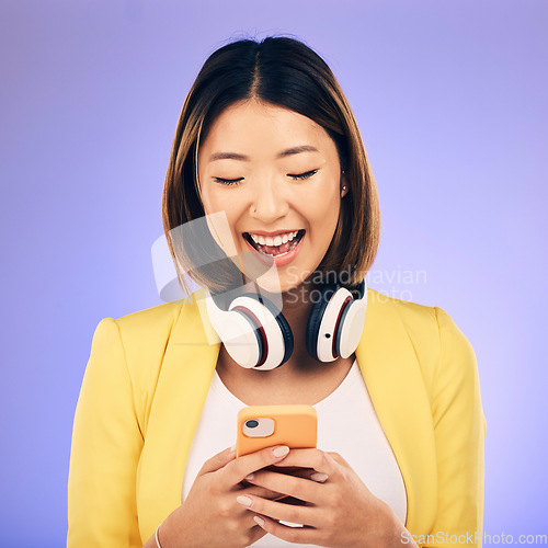 Image of Headphones, phone and happy Asian woman in studio smile for social media, internet meme and chat. Texting, smile and female person on smartphone listen to audio, song and track on purple background
