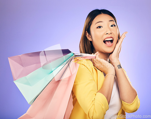 Image of Asian woman, surprise and shopping bag with retail and fashion, commercial and sale on purple background. Wow for discount at boutique, happy female customer and market with store promotion in studio