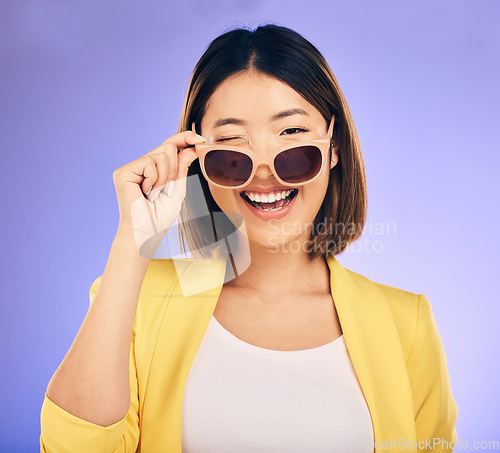 Image of Happy, portrait of asian woman wink with glasses in studio, purple background and fashion. Face, female model and blink emoji with sunglasses for secret, fun personality and gen z girl in good mood