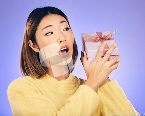 Image of Surprise, gift and box with face of asian woman in studio for birthday, celebration and curious. Thinking, wow and party with female person and present on purple background for giveaway and package