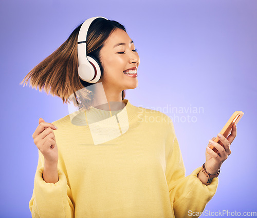 Image of Headphones, music and Asian woman dance with phone in studio for streaming, subscription and radio. Happy female person on smartphone listening to audio, song and track on purple background to relax