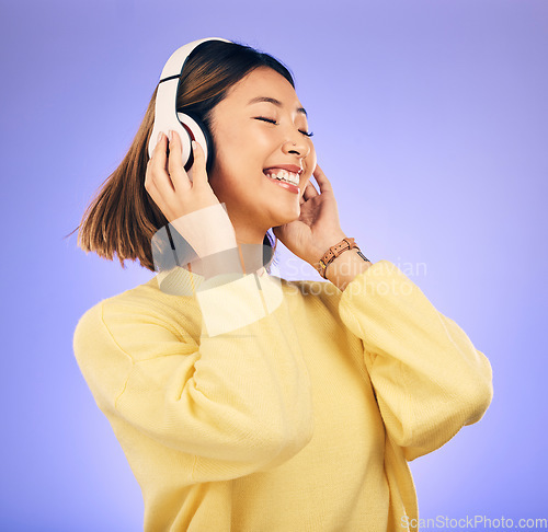 Image of Headphones, dance and happy Asian woman with music in studio for streaming app, subscription and radio. Excited, podcast and female person listening to audio, song and track on purple background