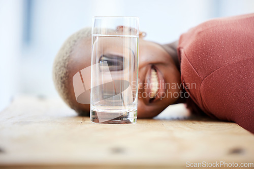 Image of Woman, funny face and water glass with big eyes, laughing and comic joke on table in apartment. African girl, crazy young student and comedy for meme with happy smile, home and playing game on desk