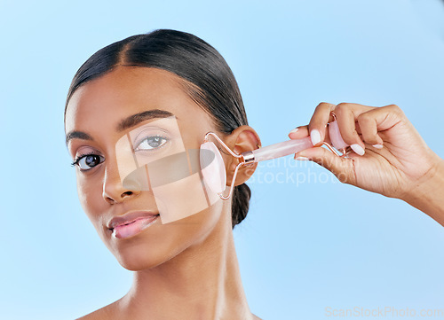 Image of Face, massage and woman with roller, beauty and skincare, natural cosmetics and tools isolated on blue background. Rose quartz, crystal and skin glow, Indian female model in portrait with dermatology