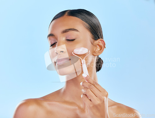 Image of Facial massage, woman and roller, beauty and skincare, natural cosmetics and tools isolated on blue background. Rose quartz, crystal and skin glow, Indian female model with dermatology and antiaging