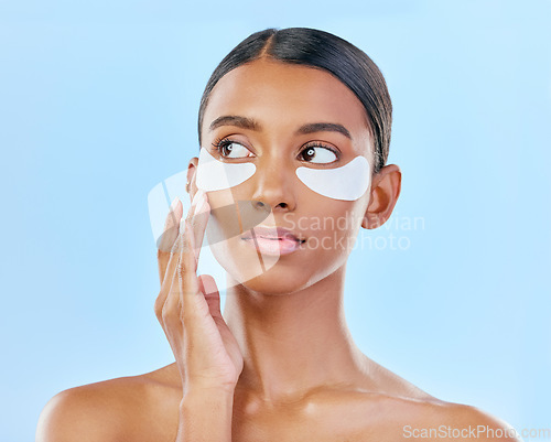 Image of Face, eye patch and beauty of a woman with natural skin glow on a blue background. Dermatology, collagen mask and cosmetics of Indian female model for facial shine, wellness or self care in studio