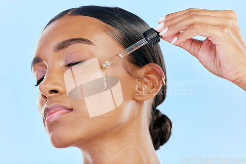 Image of Beauty, face serum and a woman with skin care on a blue background with a cosmetics dropper. Dermatology, natural glow and Indian female model for facial shine, wellness and self love in studio