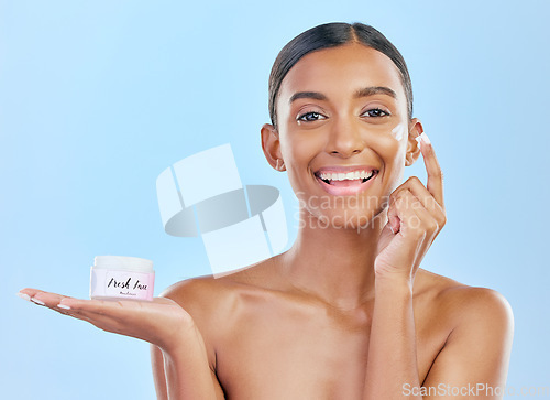 Image of Face cream, skin and beauty portrait of a happy woman with natural glow on a blue background. Dermatology, moisturizer and cosmetics of Indian female model with a product container on hand in studio