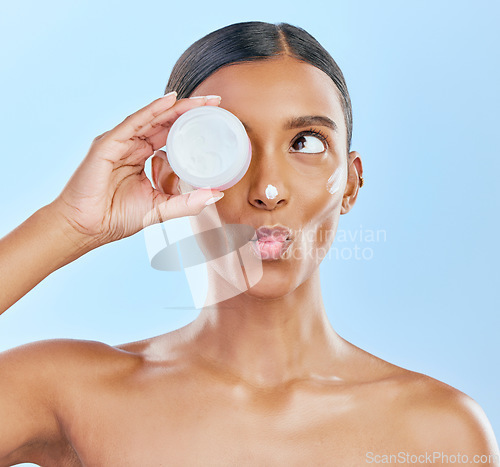 Image of Woman, face and cream jar in studio, blue background and cosmetics with kiss emoji. Indian female model, facial expression and beauty lotion in container for glow, skincare results and makeup product