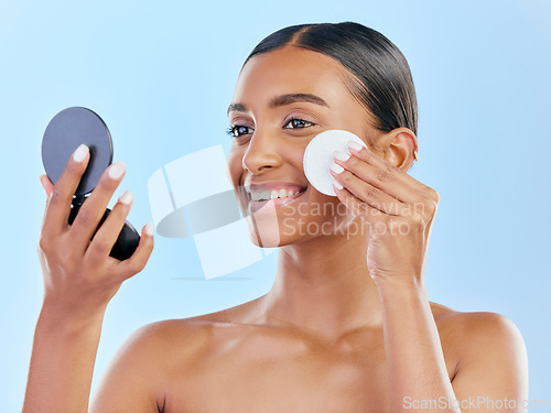 Image of Happy woman, cotton pad and skincare with mirror for makeup removal against a blue studio background. Female person with smile for beauty cosmetics, pamper or removing foundation in facial treatment