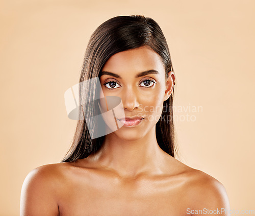 Image of Face, skin and beauty portrait of a woman with natural glow on a beige background. Dermatology, makeup and cosmetics of serious Indian female model for facial shine, hair care or self love in studio