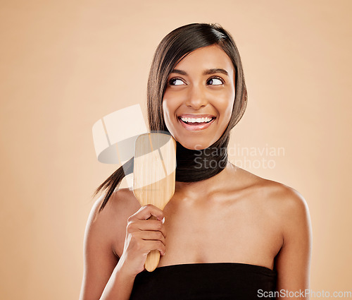 Image of Face, smile and a woman brushing her hair in studio on a cream background for natural or luxury style. Haircare, thinking and shampoo with a young indian female model at the salon or hairdresser