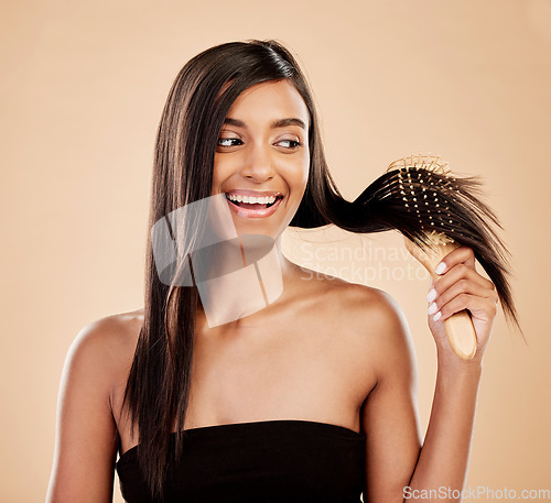 Image of Smile, beauty and a woman brushing her hair in studio on a cream background for natural or luxury style. Haircare, face and shampoo with a happy young indian female model at the salon or hairdresser