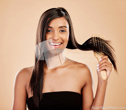 Image of Portrait, beauty and a woman brushing her hair in studio on a cream background for natural or luxury style. Haircare, face and shampoo with a young indian female model at the salon or hairdresser
