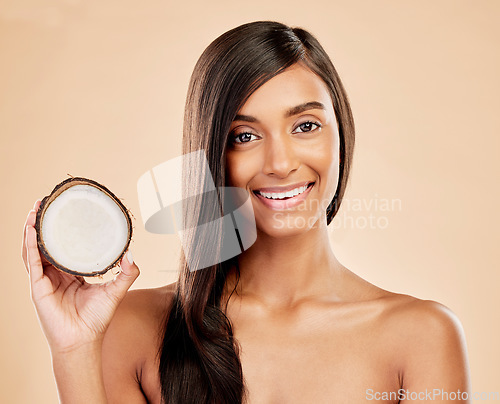 Image of Portrait, woman and coconut for hair, beauty or cosmetic treatment for natural skincare on studio background. Happy indian female model with tropical fruits for hairstyle, aesthetic benefits or shine