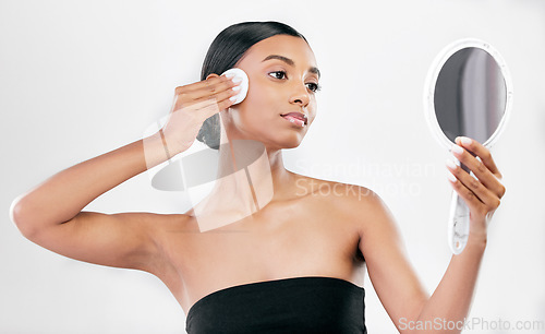 Image of Woman, mirror and cotton pad for face, cosmetics and aesthetic skincare in studio on white background. Indian female model looking at reflection with beauty product for facial cleaning or dermatology