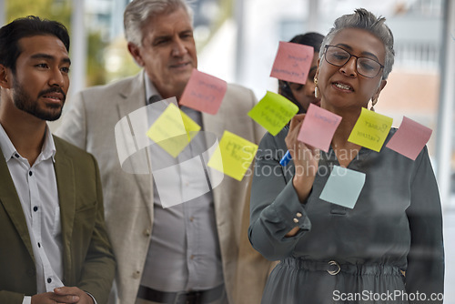 Image of Meeting, planning and glass with a senior woman leading a presentation in a boardroom for company strategy. Teamwork, presentation and sticky notes in an office with a female manager talking to staff