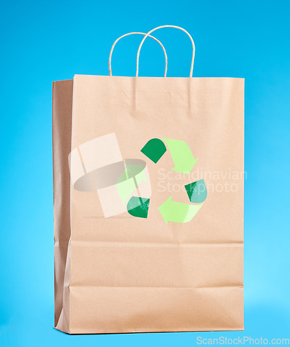 Image of Brown paper bag, recycling sign and studio for sustainability, shopping and retail package by blue background. Eco friendly product, climate change and design for social responsibility to save planet