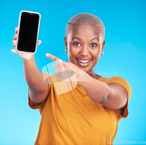 Image of Portrait, phone screen and happy black woman point at studio advertising space, online app promo or web news. Smile, smartphone UI mockup and African person gesture at mobile deal on blue background