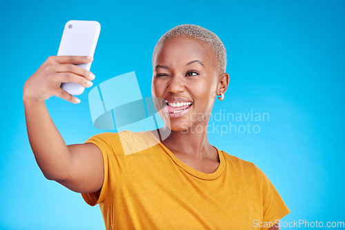 Image of Social media, selfie and funny face with a black woman on blue background in studio to update her profile picture. Post, app and a happy young female influencer taking a photograph for her status