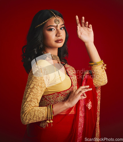 Image of Portrait, beauty and Indian woman with fashion, traditional dress and luxury against a red studio background. Face, female person and model with cultural clothes, jewellery and gold with religion