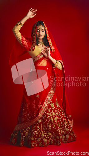 Image of Fashion, dance and Indian woman in a traditional dress, jewellery and celebration on a red studio background. Female person, girl and model with a cultural outfit, dancing and routine with confidence