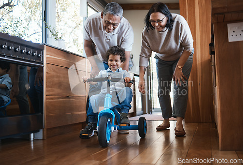 Image of Grandparents, teaching child to ride and bike in kitchen, home or childhood memory of learning with elderly people. Kid, grandmother and grandfather with bicycle and cycling on training wheels