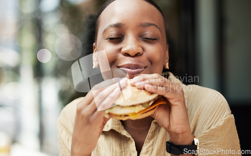 Image of Restaurant, fast food and black woman eating a burger in an outdoor cafe as a lunch meal craving deal. Breakfast, sandwich and young female person or customer enjoying a tasty unhealthy snack