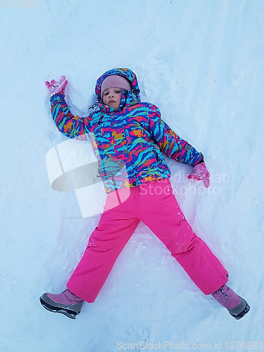 Image of Cute little kid girl in warm ski sport suit making snow angel outdoors. Kid having fun lying on snowdrift after snow storm in winter. Children outdoor activities. Winter vacation and holidays.